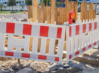 White and orange construction barrier fencing surrounding a work area with wooden panels and a small orange safety light on top (site boundary)